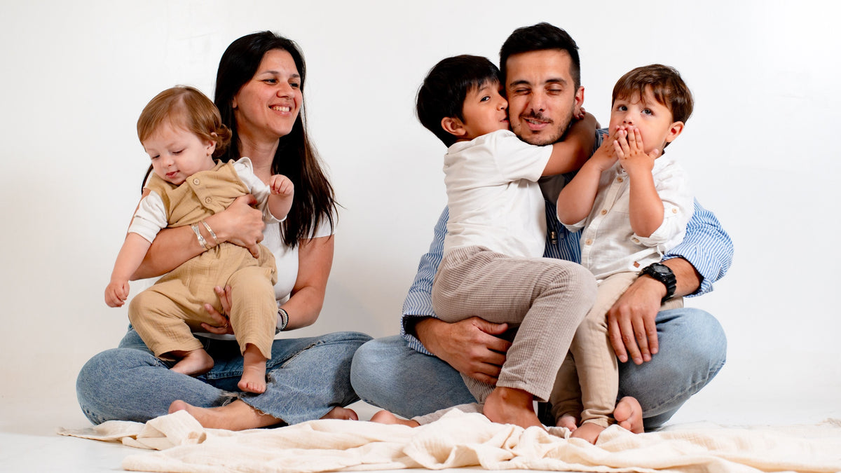 A mom and a dad are hugging their 3 children whilst sitting on the floor. Kids education, parenting goals, new year resolutions.